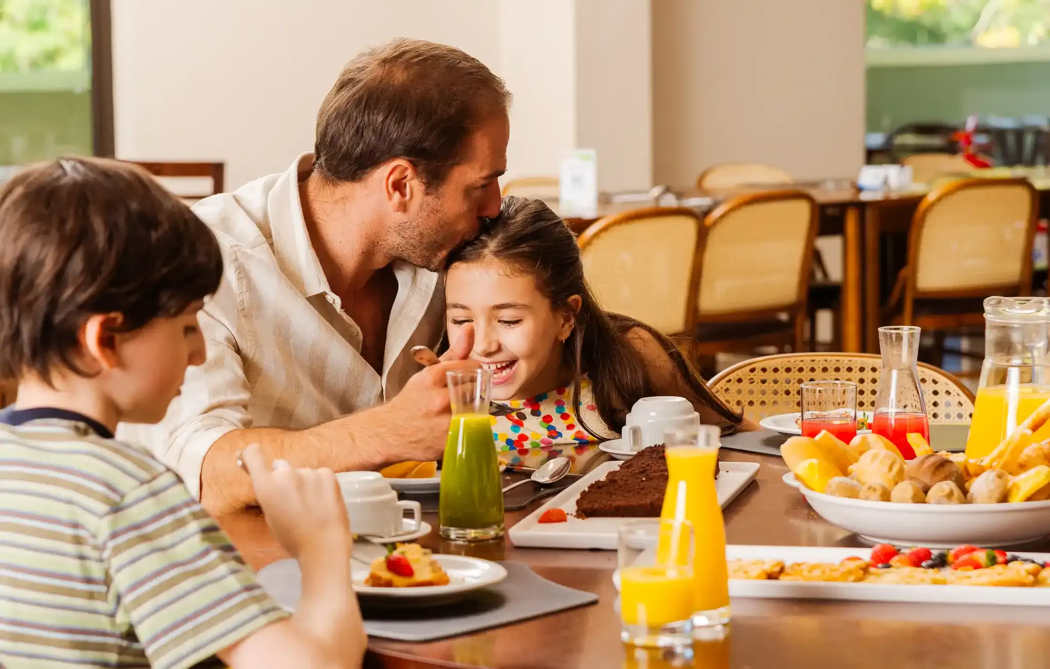 pai na mesa tomando café com os filhos e beijando a filha
